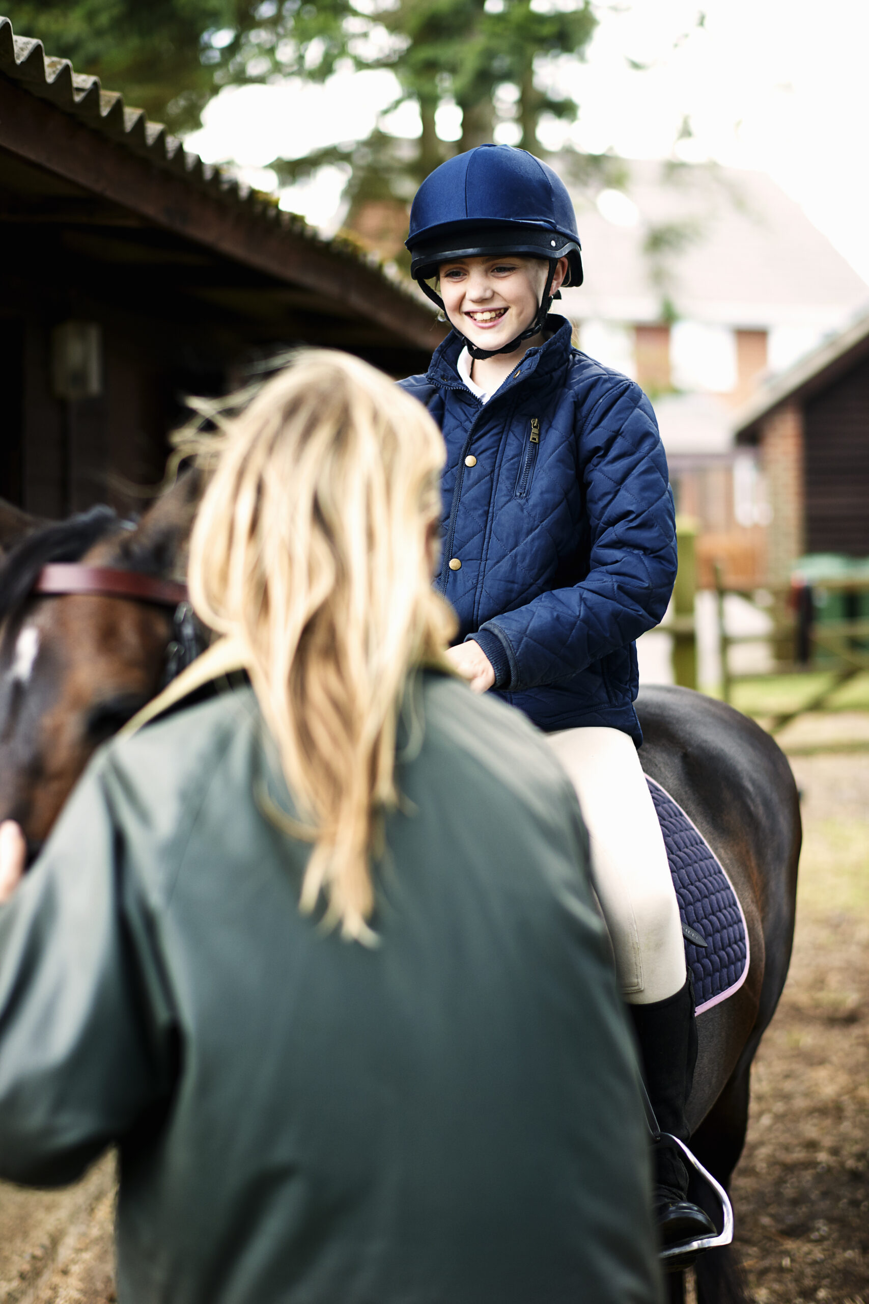 Lächelndes Kind auf einem Pony beim Reitunterricht im Stall