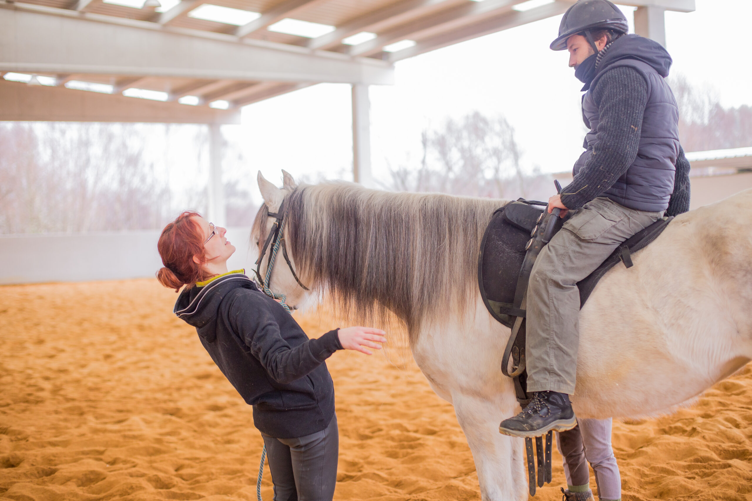 Reitlehrerin unterstützt einen Anfänger beim Reiten und erklärt den sicheren Umgang mit dem Pferd
