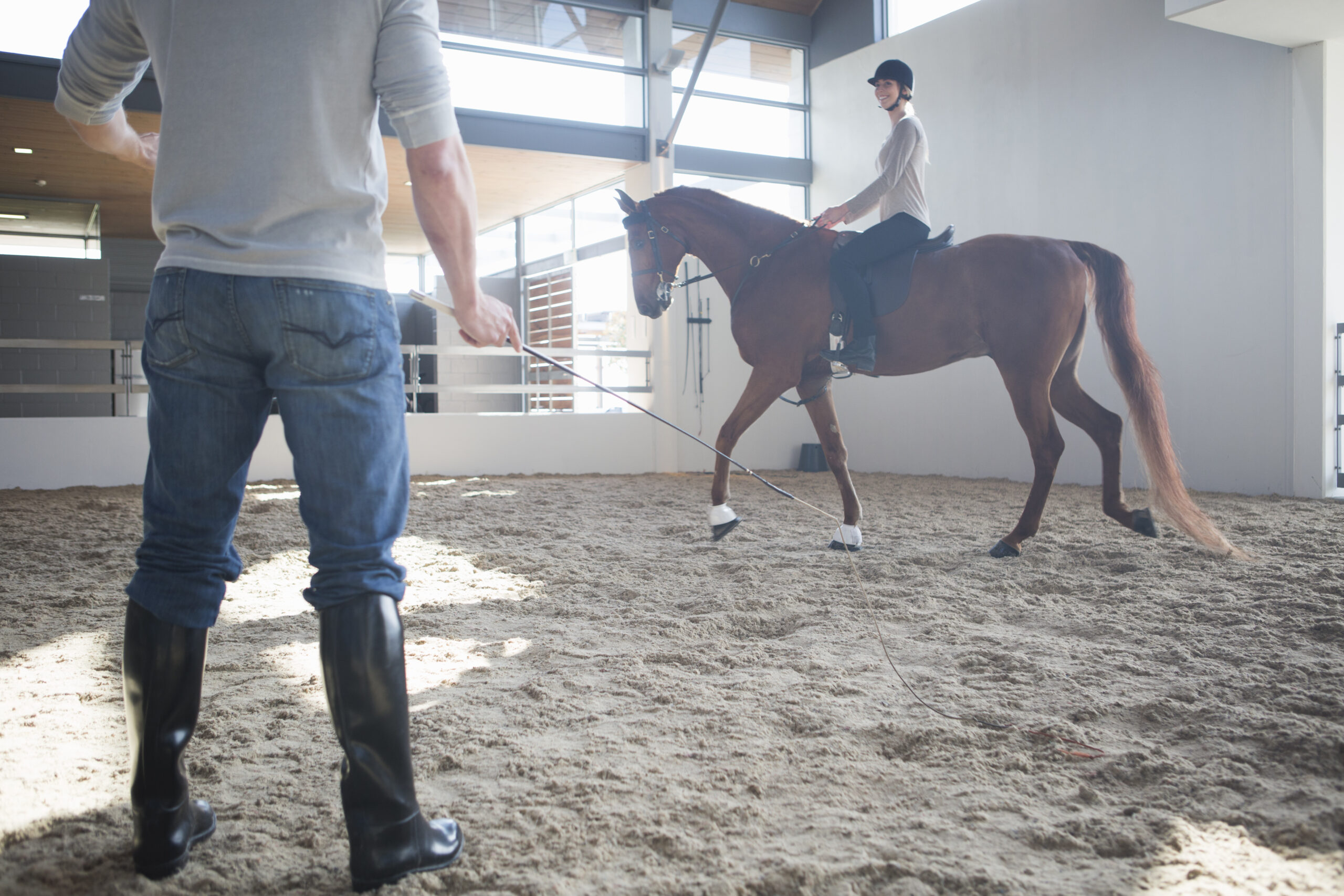 Reitlehrer gibt Longenunterricht mit einer Reitanfängerin in der Reithalle
